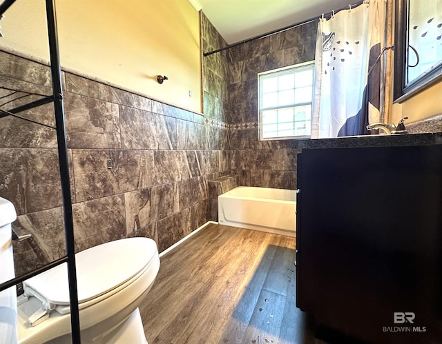 full bathroom with wood finished floors, tile walls, shower / bathtub combination with curtain, toilet, and vanity