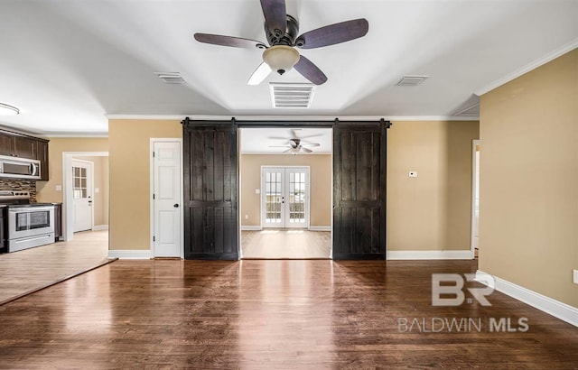 unfurnished living room with wood finished floors, a barn door, ceiling fan, and visible vents