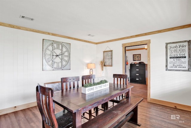 dining room with wood walls, ornamental molding, and hardwood / wood-style flooring