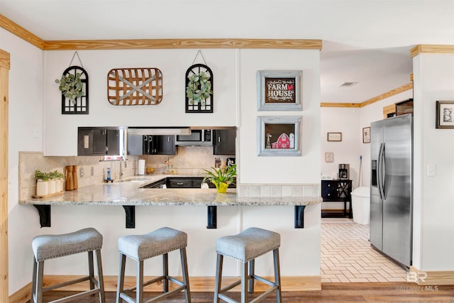 kitchen with kitchen peninsula, appliances with stainless steel finishes, backsplash, a breakfast bar, and sink