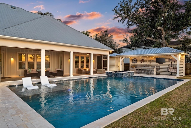 pool at dusk with a patio area and a bar