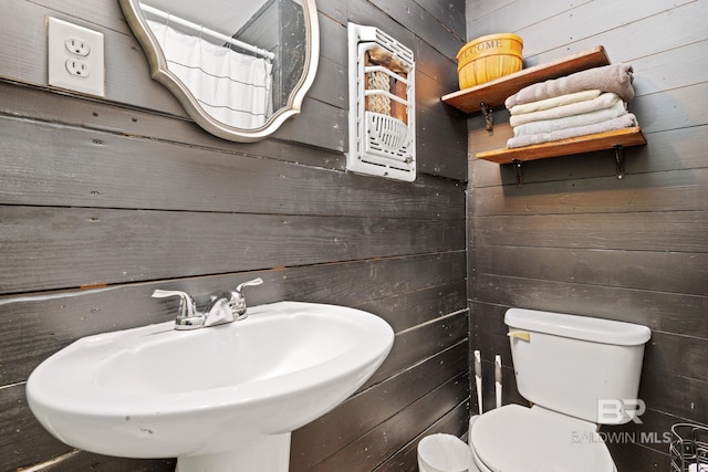 bathroom featuring toilet, sink, and wood walls