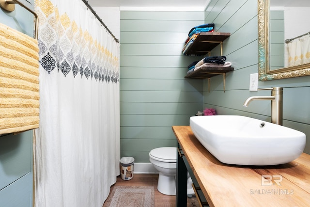 bathroom featuring wooden walls, toilet, sink, and hardwood / wood-style floors