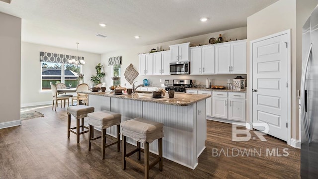 kitchen with dark wood finished floors, white cabinetry, appliances with stainless steel finishes, an island with sink, and a kitchen bar