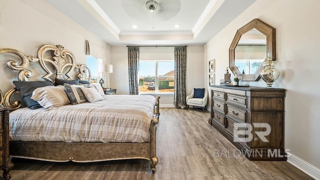 bedroom with a tray ceiling, crown molding, baseboards, and wood finished floors