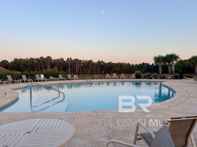 pool at dusk featuring a patio area, fence, and a community pool