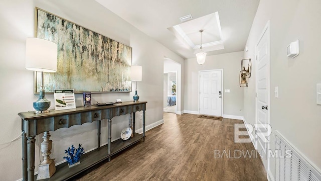 foyer entrance with a tray ceiling, visible vents, baseboards, and wood finished floors