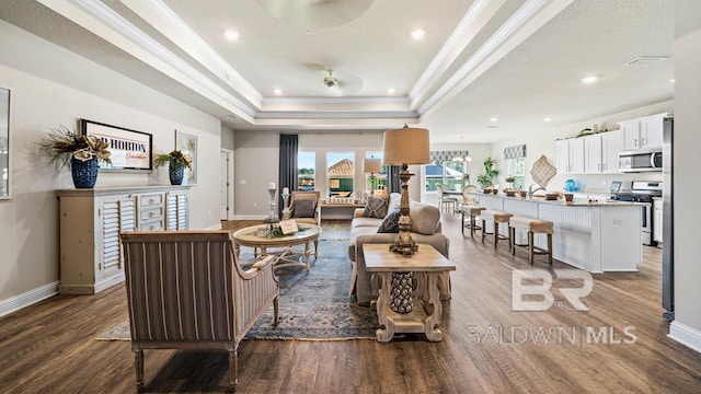 living room featuring baseboards, a tray ceiling, wood finished floors, and ornamental molding