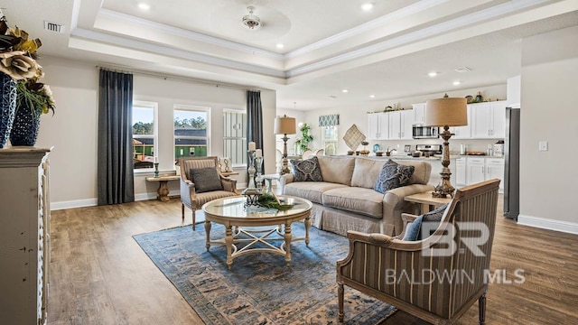 living area with ornamental molding, a tray ceiling, wood finished floors, and baseboards