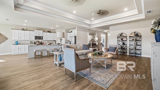 living room with baseboards, a raised ceiling, visible vents, and light wood-style floors