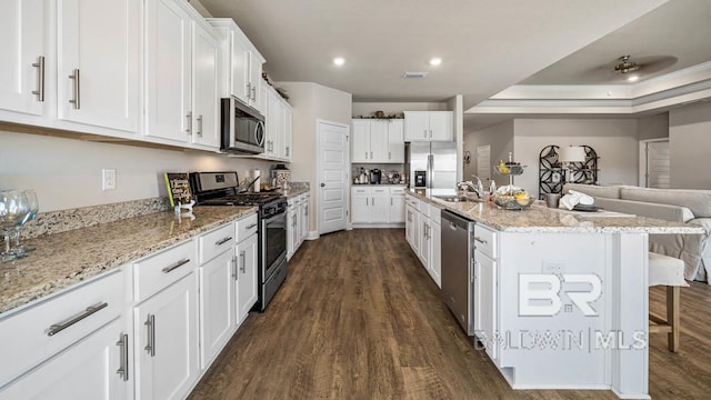 kitchen featuring stainless steel appliances, white cabinetry, a kitchen breakfast bar, open floor plan, and dark wood-style floors