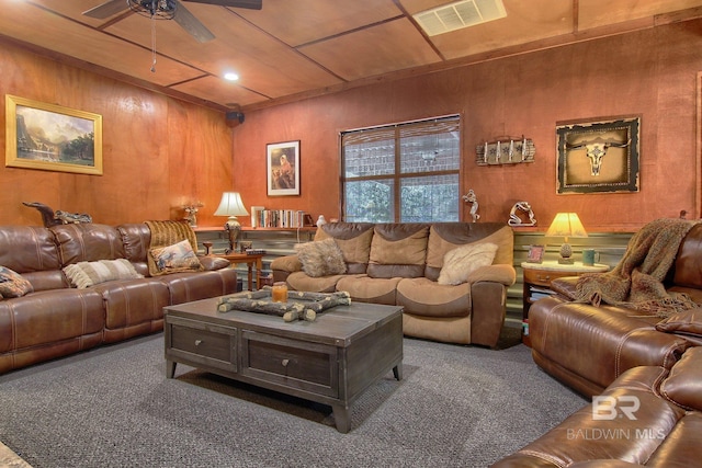 carpeted living room with ceiling fan and wood walls