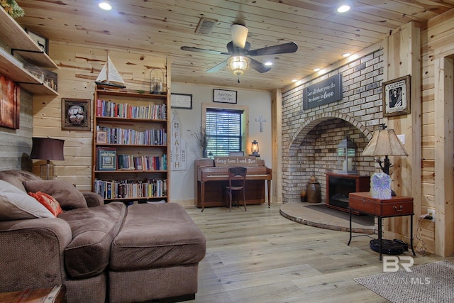 sitting room featuring light wood-type flooring, a wood stove, ceiling fan, wooden ceiling, and wooden walls