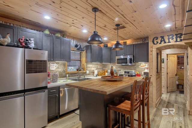 kitchen with stainless steel appliances, a center island, pendant lighting, butcher block countertops, and light hardwood / wood-style floors