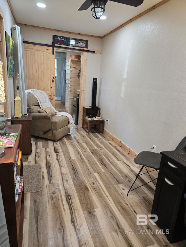 living area featuring light hardwood / wood-style floors, ornamental molding, a barn door, and ceiling fan