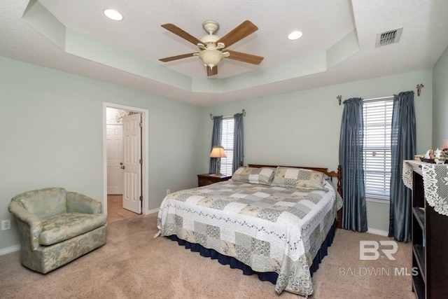 bedroom with a tray ceiling, ceiling fan, light carpet, and a textured ceiling