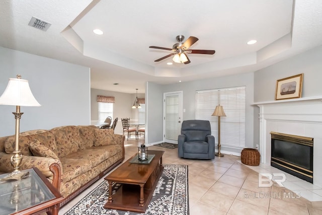 tiled living room with a fireplace, a tray ceiling, and ceiling fan