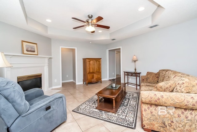 tiled living room with a tray ceiling and ceiling fan