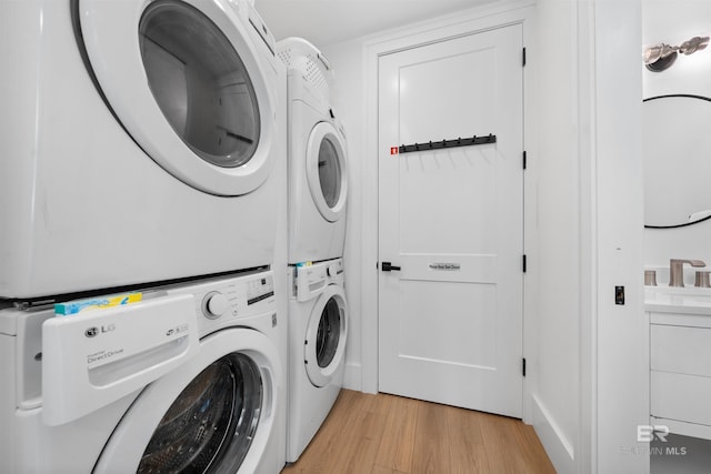 clothes washing area featuring stacked washer / drying machine, laundry area, and light wood-style floors