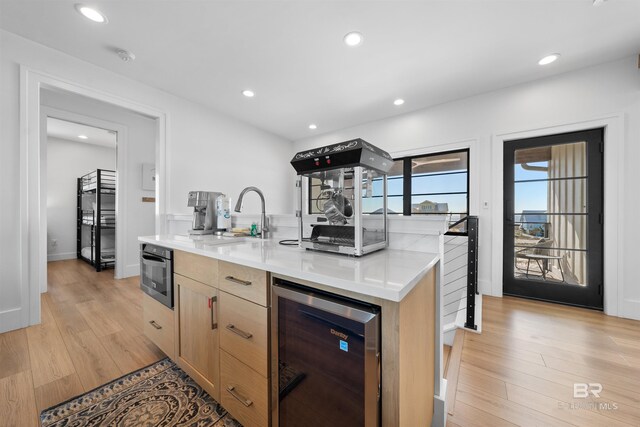 kitchen with a center island with sink, light wood-type flooring, wine cooler, and oven