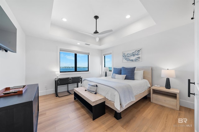 bedroom with baseboards, light wood-style flooring, and a raised ceiling