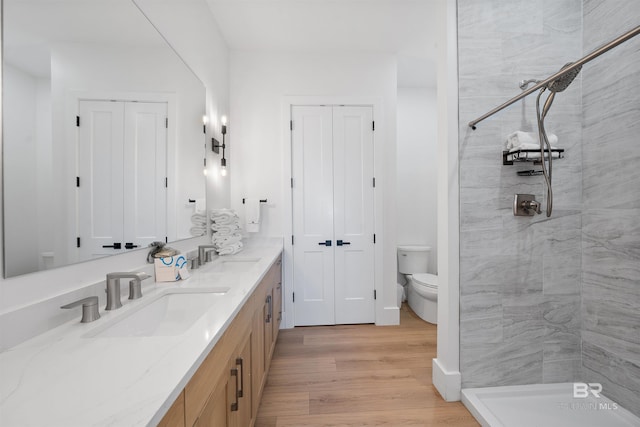 bathroom with toilet, a sink, double vanity, tiled shower, and wood finished floors