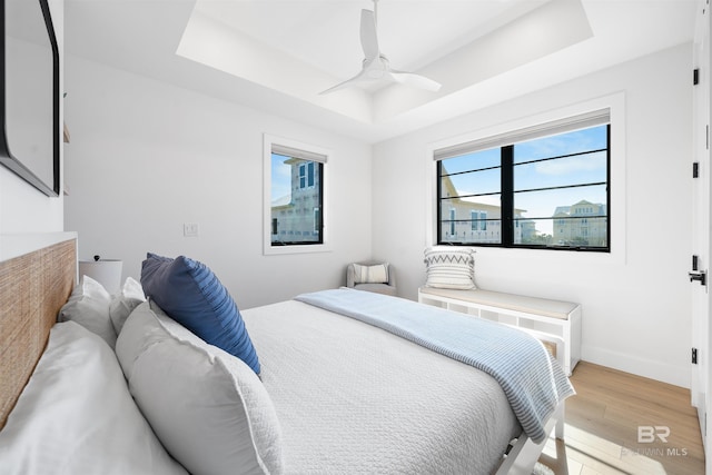 bedroom featuring baseboards, a tray ceiling, a ceiling fan, and light wood-type flooring