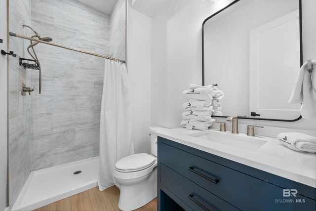 full bathroom featuring toilet, vanity, a stall shower, and wood finished floors