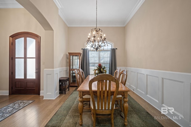 dining room featuring crown molding, arched walkways, a notable chandelier, and wood finished floors