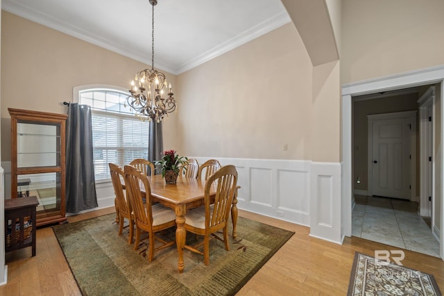 dining space with light wood finished floors, a wainscoted wall, crown molding, a chandelier, and a decorative wall