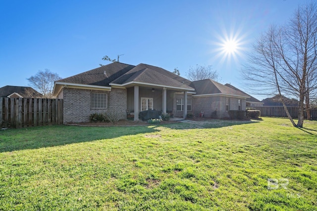 back of property with fence, a lawn, and brick siding