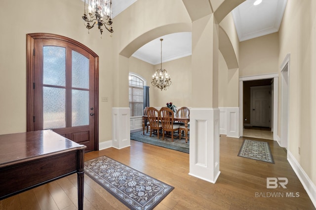 foyer featuring arched walkways, a notable chandelier, a high ceiling, wood finished floors, and crown molding