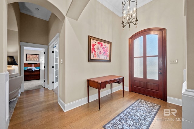 entrance foyer featuring baseboards, arched walkways, a high ceiling, light wood-type flooring, and a notable chandelier