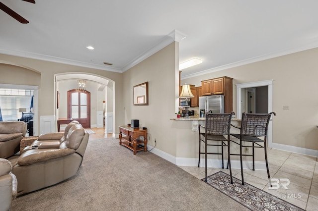 living area featuring light tile patterned floors, baseboards, arched walkways, and crown molding