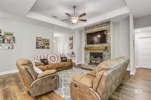 living room featuring a brick fireplace, a raised ceiling, and ceiling fan