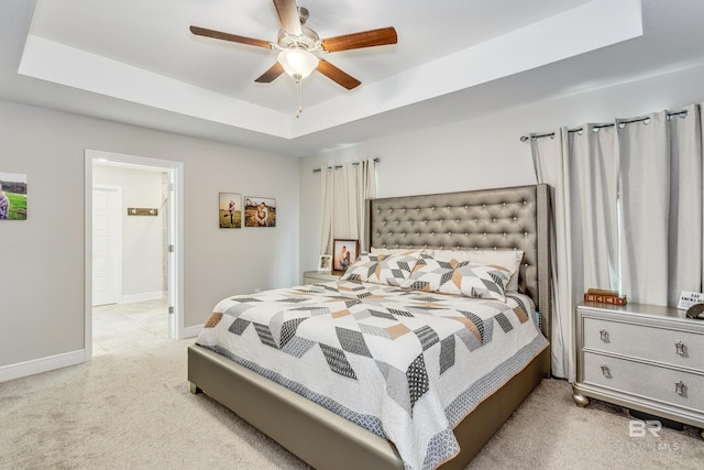 bedroom featuring ceiling fan, a tray ceiling, and light carpet