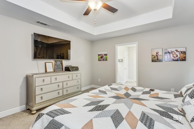 bedroom with ensuite bathroom, a raised ceiling, ceiling fan, and light colored carpet