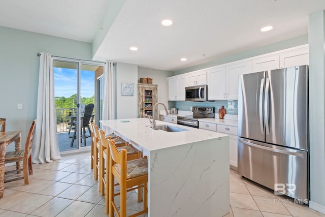 kitchen featuring stainless steel appliances, decorative backsplash, sink, a kitchen island with sink, and white cabinets