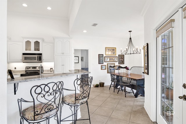 kitchen with stainless steel appliances, light stone counters, ornamental molding, white cabinets, and decorative light fixtures