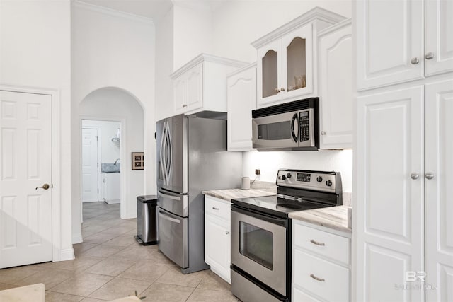 kitchen with stainless steel appliances, crown molding, light tile patterned flooring, and white cabinets