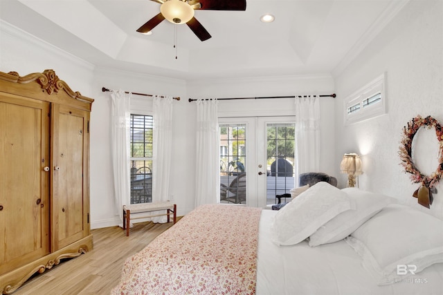 bedroom with light hardwood / wood-style flooring, a tray ceiling, multiple windows, and access to outside