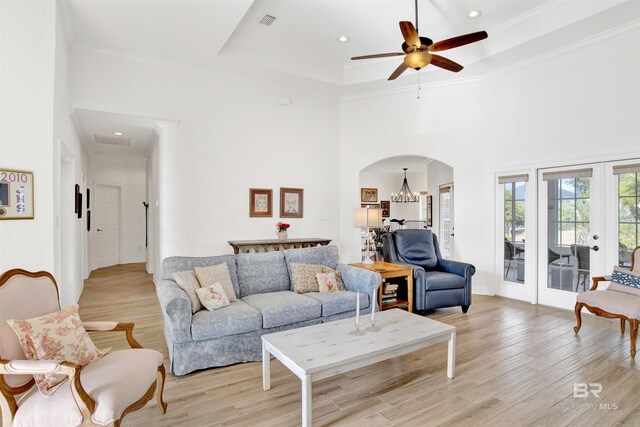 living room featuring french doors, crown molding, light hardwood / wood-style flooring, a tray ceiling, and a high ceiling