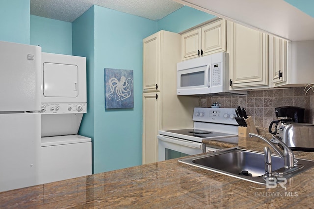 kitchen with sink, white appliances, stacked washing maching and dryer, cream cabinets, and decorative backsplash