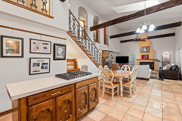 kitchen featuring light tile patterned floors, tile counters, high vaulted ceiling, and stainless steel gas cooktop