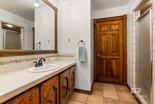 bathroom with vanity, a textured ceiling, backsplash, a shower with shower door, and tile patterned floors