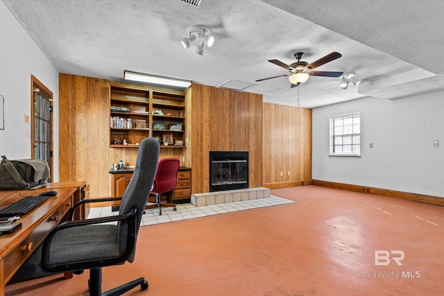 office area with a textured ceiling, a fireplace, wood walls, and ceiling fan