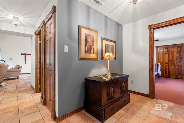 hall with a textured ceiling and light tile patterned floors