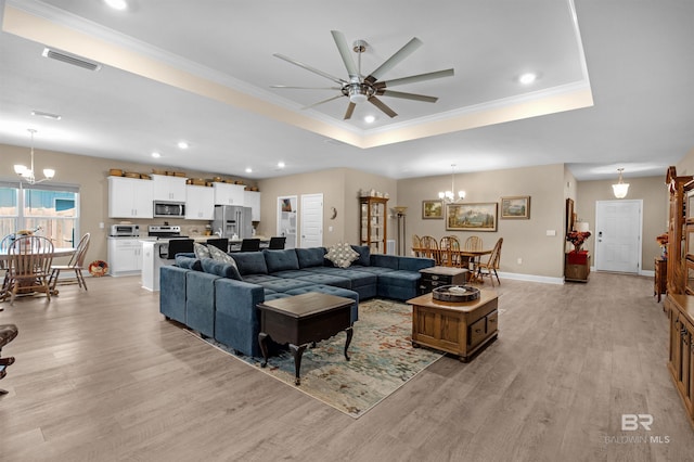 living room featuring ornamental molding, ceiling fan with notable chandelier, light hardwood / wood-style floors, and a raised ceiling