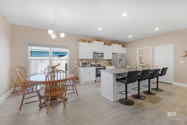 kitchen with appliances with stainless steel finishes, a kitchen breakfast bar, an island with sink, light stone counters, and white cabinetry