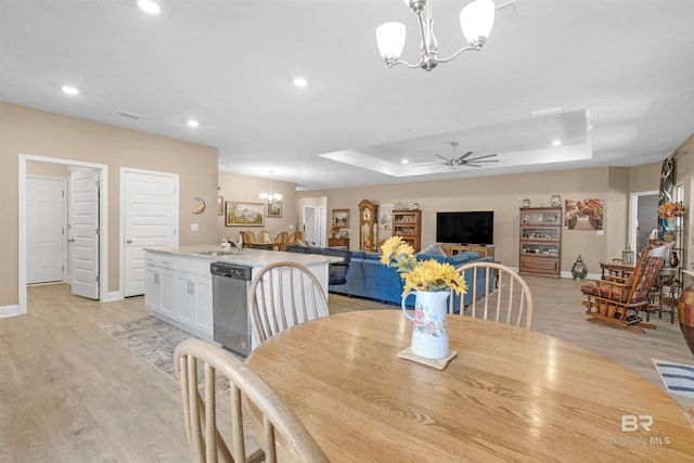 dining space featuring ceiling fan with notable chandelier, light hardwood / wood-style flooring, and a raised ceiling